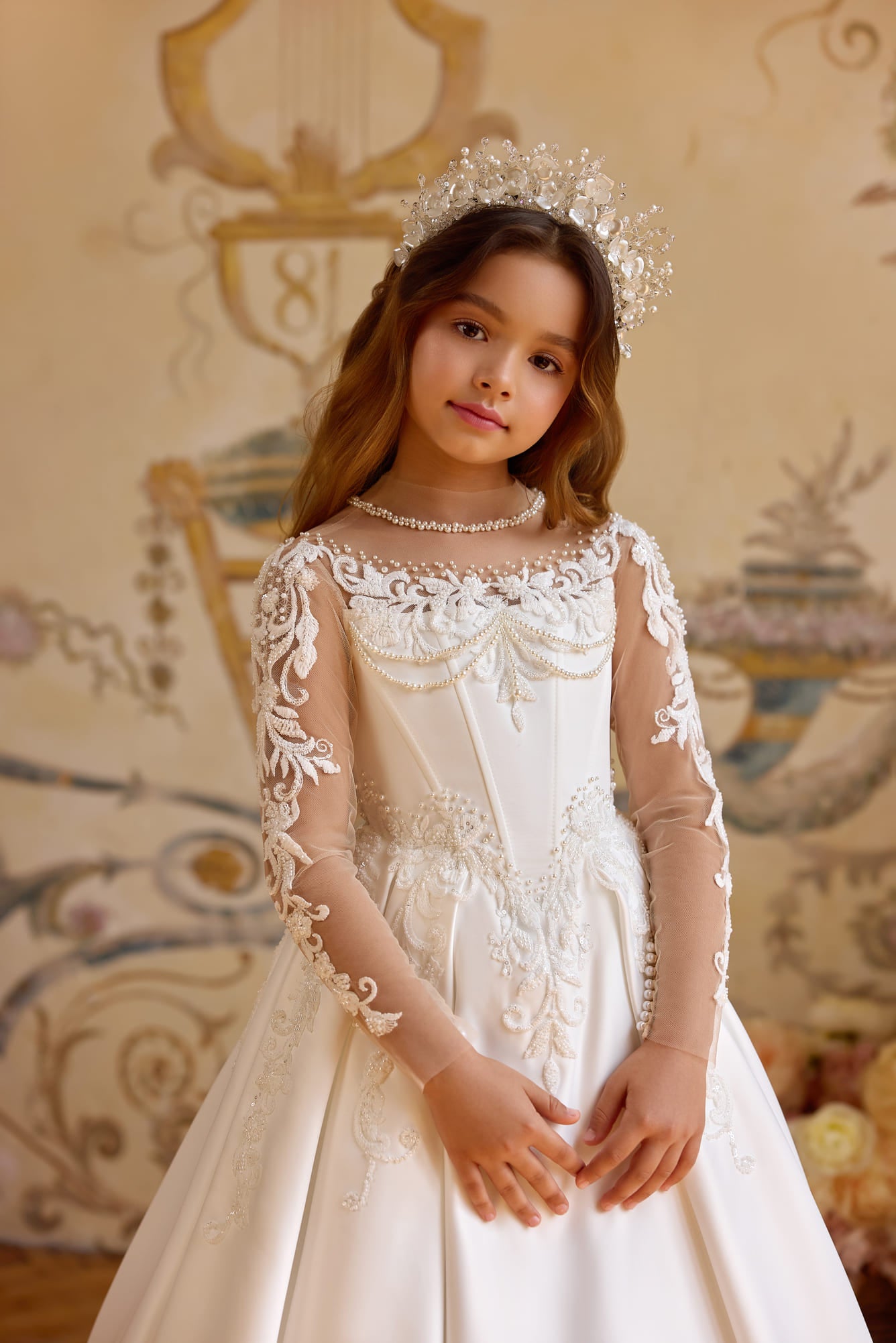 Girl wearing an embroidered First Communion dress with pearl details and sheer illusion neckline