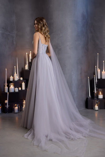 A model wearing a floor-length silver grey corset gown with a sequin bodice, illusion insert, and flowing tulle skirt, styled for prom or formal evening wear.