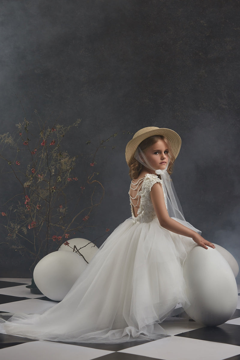 Young girl in Girls Open Back Tulle High-Low Dress and hat sitting on large white balls against a dark background