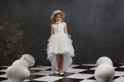 Young girl in Girls Open Back Tulle High-Low Dress and hat standing on a checkered floor with large eggs around.