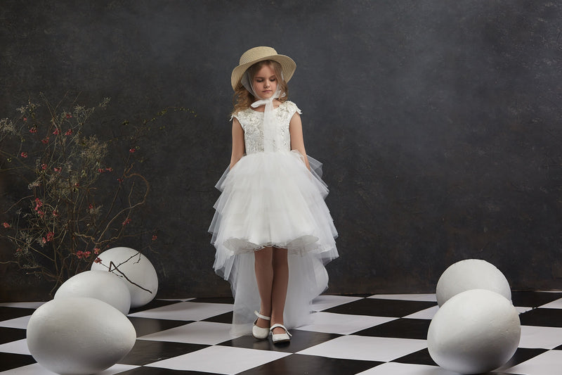 Young girl in Girls Open Back Tulle High-Low Dress and hat standing on a checkered floor with large eggs around.