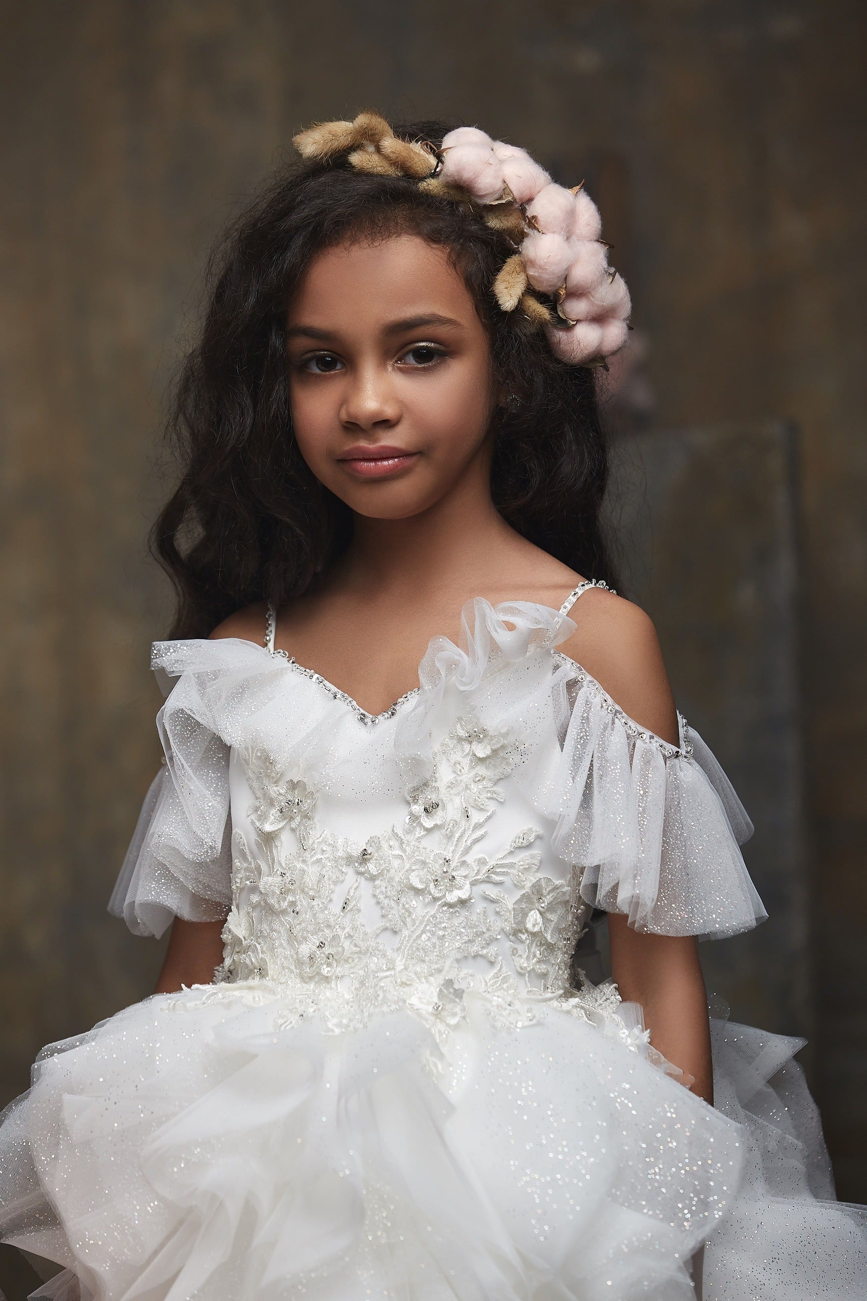 Young girl in Girl's Ruffled Sparkly Long Princess Dress with a flower crown against a brown background