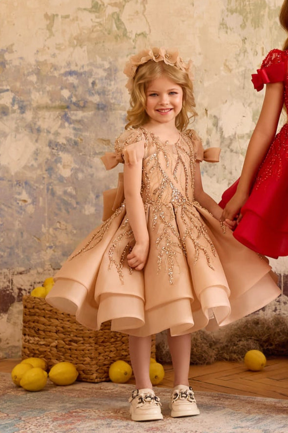 Girl wearing cappuccino sequin bow dress with puff sleeves and layered skirt