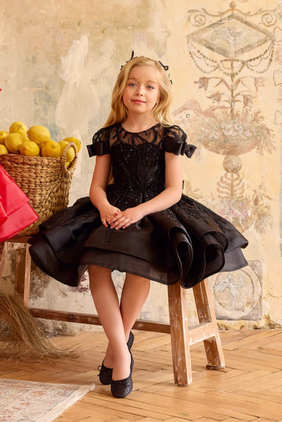 Girl wearing black sequin bow dress with puff sleeves and layered skirt