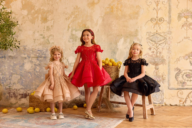 Three young girls in red black and cappuccino dresses standing in a room with decorative elements.