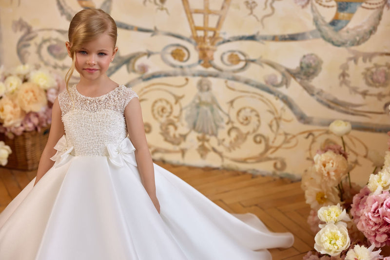 Girl wearing pearl embellished Communion dress with bow waist