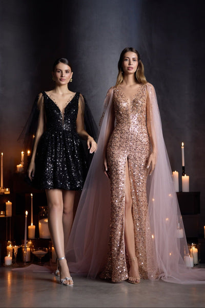 A model wearing a short black sequin prom dress with sheer cape sleeves and a deep V-neckline, styled for a cocktail or formal event.