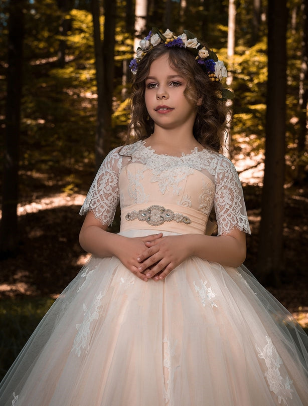Young girl in Verona Blush Flower Girl Tulle Dress with a floral crown standing in a forest.
