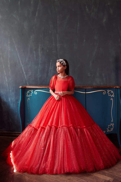 Girl wearing an elegant red Christmas party dress with puff sleeves and sparkling tulle skirt, standing in front of a vintage blue dresser by Mia Bambina Boutique
